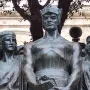 Great Siege Monument with three bronze draped figures on a white base beside a street lamp and cannon.