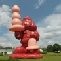 A massive inflatable Santa Claus stands on a grassy lawn holding a large pink object, with another pink object near its left leg.