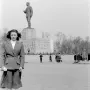 The Stalin Monument rises on a tall pedestal in a large square, with a woman posing in the foreground and people nearby.