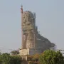 Statue of Belief under construction, draped in scaffolding and protective netting with a crane beside it.
