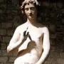 Adam statue with curly hair, one hand raised and the other holding leaves over his lower body.