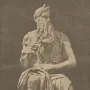 Seated statue of Moses with a long curly beard, horns, and tablets under his arm.
