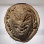 White circular relief sculpture of the Head of a Faun with a grinning face, pointed ears, and curly beard and hair.