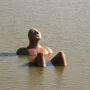 Hombre Río sculpture emerging from calm water with a peaceful face.