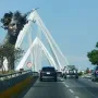 Reminiscencia, a dark bust of a woman crowned with flowers and spiky elements, set before a white cable-stayed bridge.