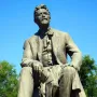 The Chekhov monument shows a bronze seated figure holding a book on a dark granite pedestal in a park.