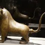 The Lion of Monzon sculpture shown from a three-quarters angle, with engraved decorative patterns across its body.