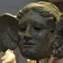 Bronze head of Hypnos with a wing on the side, showing a tranquil face with wavy hair and a weathered surface.