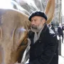 Arturo Di Modica stands beside the Charging Bull sculpture, touching its snout.