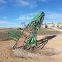 Carhenge-like roadside monument with cars arranged on gray supports behind a large green metal sculpture in the foreground.