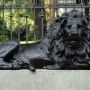 Guarding Lion sculpture on a concrete pedestal in front of an ornate fence and brick pillar.