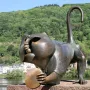 Heidelberg Bridge Monkey sculpture crouching on a stone ledge, holding a round disk with the river and wooded hill behind it.