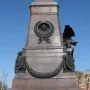 Lower section of the Monument of Alexander III with a bronze bust relief, draped garland, and a winged eagle on a granite pedestal.