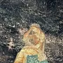 A seated figure in golden robes rests on a patterned blue-green omphalos with a dark background.