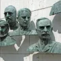 Four bronze busts from the Polio Hall of Fame mounted on a light stone wall, with part of a fifth bust visible.