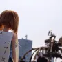 Doll with reddish-brown hair and a Japanese sign in front of La Princesse, with the large mechanical spider blurred in the background.