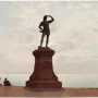 Leif, the Discoverer statue on an ornate pedestal overlooking the water, with two people seated nearby.