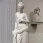 Pandora marble statue of a standing woman holding a small object, with drapery around her lower body.