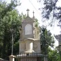 Stone monument from the Monumental Rosary of Montserrat with a central religious relief, a dove, and a cross above it, surrounded by a low fence.
