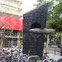 Monument to Narcís Monturiol with a scale submarine model emerging from a dark concrete base, with bicycles in front and a scaffolding-covered building behind.