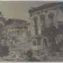 John of Austria statue on a tall pedestal amid rubble beside a damaged building