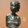 The Nubian Woman bronze bust with braided hair, earrings, and a draped garment.