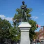 Appomattox bronze statue of a man with crossed arms on a tall stone pedestal in a street