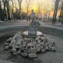 Fisherman Fountain statue in a park at sunset, with a man wrestling a snake in the center of a dry circular basin.