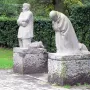 The Mourning Parents sculpture with two kneeling stone figures on separate pedestals outdoors.
