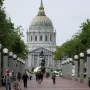 Pioneer Monument on a granite base in a brick-paved plaza, with San Francisco City Hall and its dome in the background.