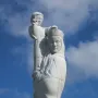 Detail of Our Lady of the Isles showing a crowned, veiled figure supporting a smaller figure against a blue sky.