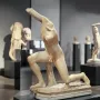 Subiaco Ephebe, a pale stone kneeling male sculpture displayed on a dark pedestal in a museum gallery.
