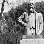 Monument to Ernesto Teodoro Moneta on a tall stone pedestal in a park, with trees and people on the lawn behind it.