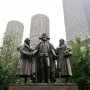 Heald Square Monument bronze sculpture of three historical figures on a red granite pedestal, with downtown skyscrapers behind it.