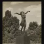 The Dancing Girl sculpture stands on a tall pedestal outdoors among trees.