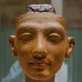 Unfinished head of Nefertiti with closed eyes and a rough top edge.