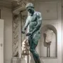 Bronze statue of the Athlete from Ephesus standing on a pedestal in a museum gallery.