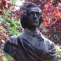 Frederic Chopin bust on a stone base, set against foliage with red and green leaves.