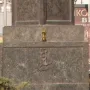 Stone base of the Statue of Sofia with a carved cross-and-anchor emblem and a small vessel on the ledge above it, partly obscured by foliage.