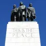 The This Is the Place Monument with three bronze men standing on a stone pedestal against a blue sky.