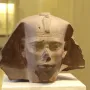 Weathered stone head of the Djedefre sphinx with a damaged nose and royal headpiece featuring a cobra emblem.