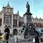 Adam Mickiewicz Monument on a tall pedestal in Krakow’s market square, with the Cloth Hall and people in the background.