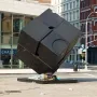 The Alamo black cube sculpture in a city street, with a person lying on its base.