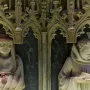 Two carved stone figures in Gothic niches from the Tomb of Charles III and Eleanor, one wearing a wide-brimmed hat and the other reading a book.