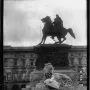 Victor Emmanuel II Monument with an equestrian statue above a carved pedestal, a crowned lion below, and a building in the background.