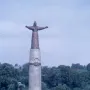 Mother Patroness monument in Cheboksary, a robed bronze figure with outstretched arms atop a tall pillar above landscaped steps and lawns.
