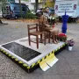 Peace Statue showing a bronze girl seated barefoot on a stool beside an empty wooden chair, holding a bouquet of flowers.