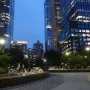 The Vessel partially visible among trees and illuminated skyscrapers at twilight.