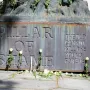 The Pillar of Shame base with white roses and candles arranged around the memorial inscription.