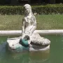 Weathered stone mermaid statue in a rectangular pool with murky green water, holding a turquoise object in her lap.